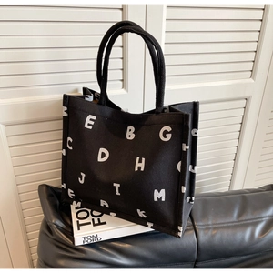 Close-up of black canvas tote bag with white letter print on a stylish leather sofa