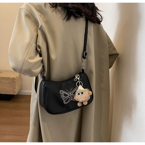 Sac demi-lune noir avec broderie nœud et pendentif peluche porté par un mannequin