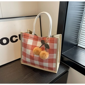 Detail of red and white checkered linen tote bag with woven handles and cherry pendant