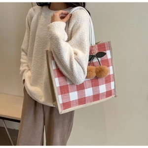 Close-up of red and white waffle tote bag with cherry pompom charm on model
