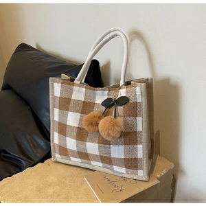 Detail of checkered linen tote bag with cherry plush charm on stone base