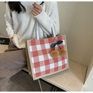 Detail of red waffle weave tote bag with woven rope handles and cherry charm decoration