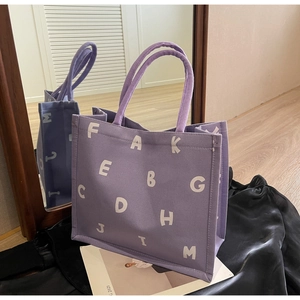 Detail view of purple canvas tote bag with white letter print and rope handles on black leather