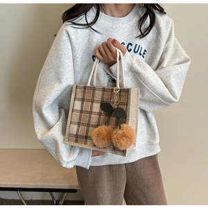 Detail of a brown plaid tote bag with plush cherry charm and white cotton rope handle