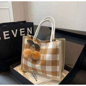Detail of checkered linen tote bag with plush cherry charm in a premium gift box
