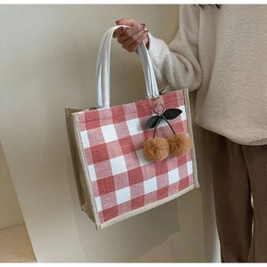 Detail shot of a red and white waffle tote bag with a cute plush cherry pendant charm