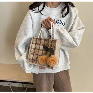 Detail of checkered canvas tote bag featuring brown plush cherry charms and cotton rope handles