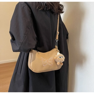 Détail du sac à bandoulière kaki avec broderie papillon rose et breloque pelucheuse