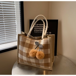 Detail view of large waffle tote bag with braided handles and cherry plush charm accessory