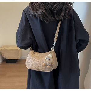 Détail du sac à bandoulière en cuir beige avec broderie papillon et pompon pelucheux