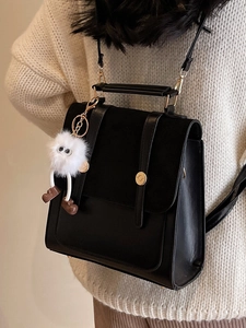 Vintage black leather backpack with fuzzy monster charm worn over white knit sweater