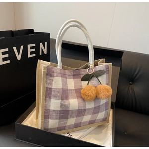 Detailed shot of purple checkered linen tote bag with plush cherry charm inside a black gift box
