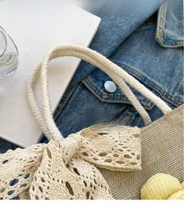 Detail of beige straw handbag with lace bow, floral charms and rope handle