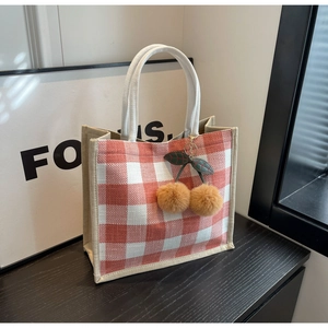 Close-up of pink waffle tote bag with cherry plush charm on wooden surface