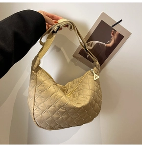 Detailed close-up of beige quilted crossbody dumpling bag with triangle zipper pull