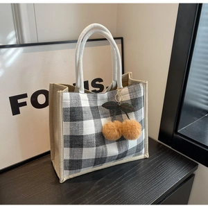 Detail of waffle pattern tote bag with woven handles and brown cherry plush pendant