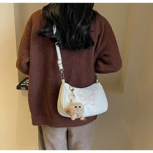 Détail d'un sac bandoulière blanc à broderie nœud avec un porte-clé en peluche porté par un mannequin