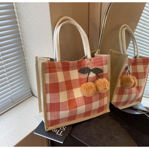 Detail of waffle-textured orange plaid tote bag with braided handles and cherry charm
