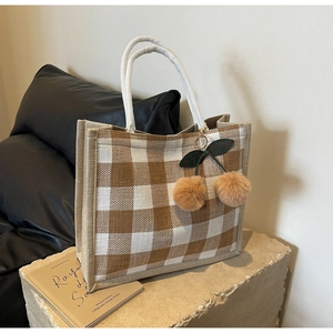 Detail of waffle plaid tote bag featuring thick cotton rope handles and cherry pendant