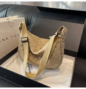 Detail of beige quilted dumpling bag featuring diamond stitching and wide strap in gift box