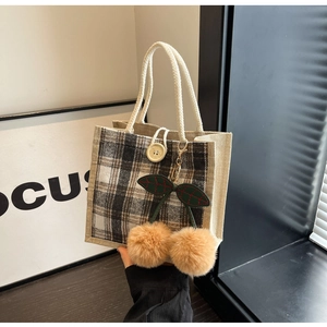 Detail of checkered woven tote bag featuring decorative plush cherry pendant and rope handle