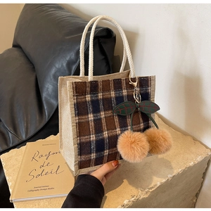 Detail of checkered canvas lunch bag with woven handles and plush cherry ornaments