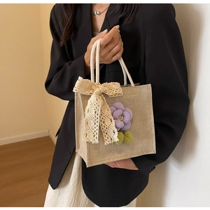 Close-up of linen handbag with beige lace bow and 3D floral detail held by a model