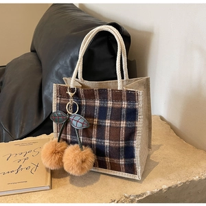 Close-up of plaid fabric tote bag with rope handles and plush cherry keychain detail