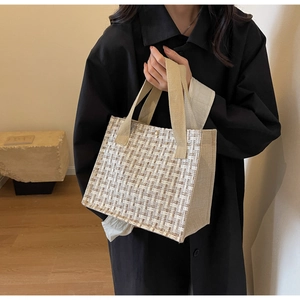 Detail of plaid woven tote bag with canvas handles held by a woman in black coat