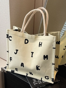 Large beige canvas tote bag with black letter print and woven handles for commute