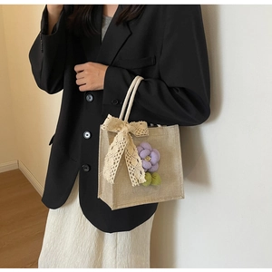 Close-up of linen handbag featuring a beige lace bow and a purple fabric flower detail