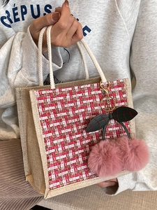 Linen tote bag with red plaid wool front and cherry plush charm held by a model