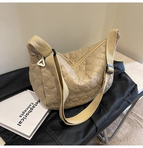 Detail showing beige quilted dumpling bag with wide canvas strap on a black background