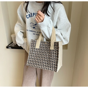 Close-up of a tweed checkered tote bag with wide beige handles and woven fabric details