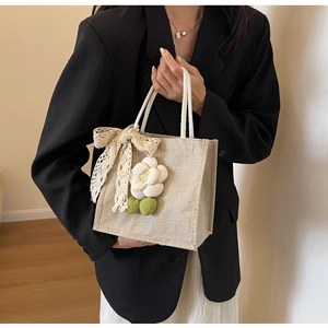 Close-up of beige linen handbag with lace bow detail and floral charm accessory