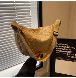 Close-up of beige quilted crossbody bag with adjustable wide strap and crescent shape