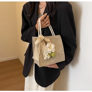 Close-up of beige linen handbag featuring decorative fabric flower and white lace bow