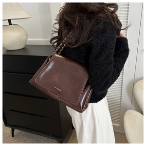 Sac fourre-tout en cuir verni marron foncé avec bandoulière chaîne porté par un modèle