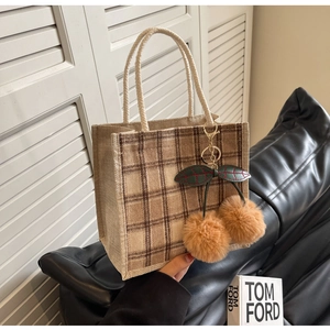 Detail of retro checkered tote bag featuring a plush cherry charm and woven rope handles
