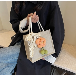 Close-up of linen handbag featuring orange floral accents and delicate lace bow details