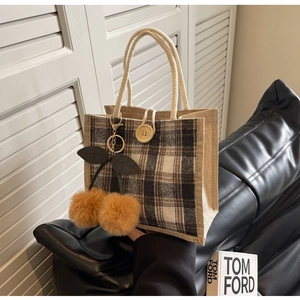 Detail of checkered tote bag featuring a yellow plush cherry charm and cotton rope handle