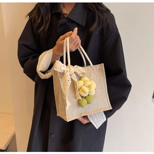 Detail of beige linen tote bag with yellow 3D flower and white lace bow handle