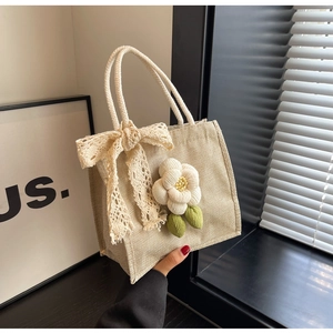 Close-up of beige linen handbag featuring lace bow and camellia floral accessory