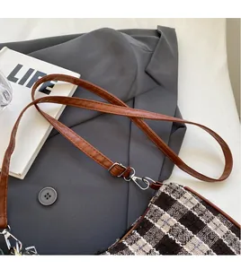 Detail of adjustable brown leather strap and silver metal buckle on a plaid crossbody bag