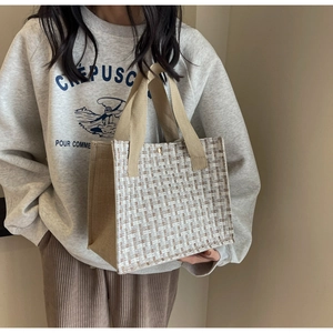 Detail of a woven tweed tote bag with khaki canvas handles shown on a model