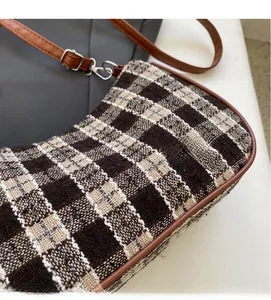 Detail of plaid woven fabric texture and brown leather strap on retro shoulder bag