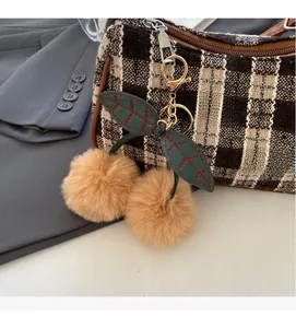 Detailed view of cherry-shaped plush charm with green leaves on a checkered handbag