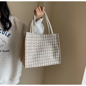 Close-up of woven tote bag with beige tweed texture, rope handles and metal clasp
