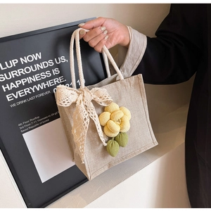 Close-up of beige linen tote bag featuring delicate lace bow and yellow fabric flower charm