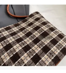 Détail du tissu en tweed à carreaux marron et de l'anse en cuir d'un grand sac cabas